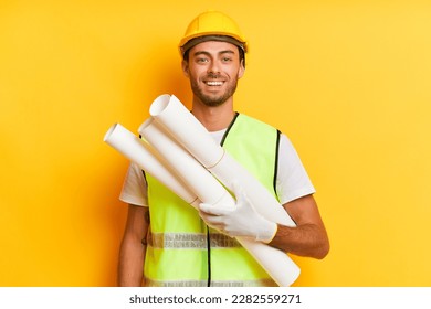 Portrait photo of young bearded man wearing yellow hard hat and holding rolls of paper, standing isolated over yellow backdrop and smiling, professional people concept, copy space, high quality photo - Powered by Shutterstock