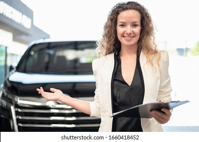 Portrait Photo Of Young Professional Look Automobile Sales Agent Standing In Front Of New Car For Sale At Modern Vehicle Showroom. Automotive  Business Concept.
