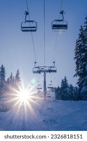 Portrait photograph of blue skies and starburst sun flare and chairlift on a winter day. Snow surrounds the ski lift in ski resort of Avoriaz, in the Portes du Soleil, France