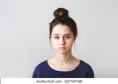 portrait of a pimply teenage girl in a blue T-shirt on a gray background, sad face