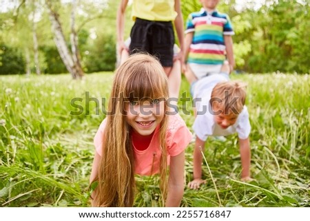 Portrait of playful girl playing with friends during wheelbarrow race competition in garden