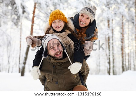 Portrait of playful happy family in winter forest looking at camera and smiling, copy space