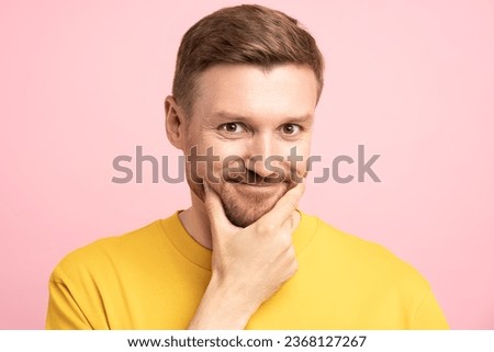 Portrait of playful man with sly insidious look touching chin by hand looking at camera isolated on pink studio background. Bearded smiling guy flirting, dodgy shifty slippery person for advertising.