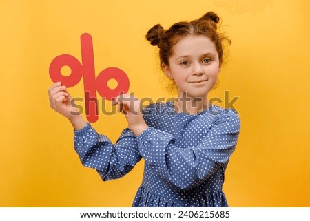 Portrait of pleasant happy preteen girl child holding red percent mark, expressing positive emotions, presenting discounts, posing isolated over yellow color background wall in studio. Sale concept