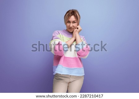 portrait of pleasant shy blond young woman in casual outfit smiling on purple background with copy space