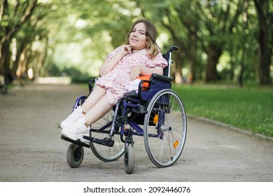 Portrait of pleasant young woman with spinal muscular atrophy smiling on camera among green summer park. Female person who using wheelchair. Concept of people with disability. - Shutterstock ID 2092446076