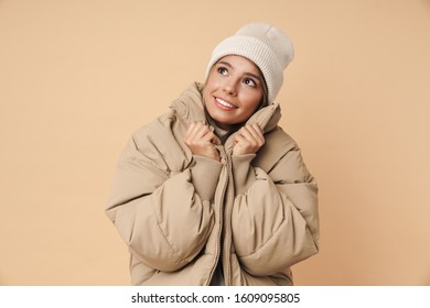 Portrait Of Pleased Young Woman In Winter Coat Smiling And Looking Upward Isolated Over Beige Background