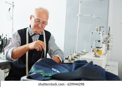 Portrait Of Pleasing Old Man Working In Tailoring Studio Making Clothes At Sewing Machine And Hand Stitching Cloth