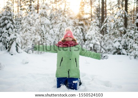 Portrait of plump funny girl in winter clothes throwing up snow in forest