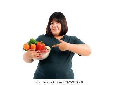 Portrait of a plump girl wearing a gray t-shirt holding fresh vegetables on a white background. Selective focus. - Shutterstock ID 2145240509