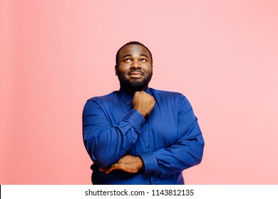 Portrait of a plus size man in blue shirt looking up with arms crossed, isolated on pink background