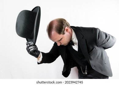 Portrait of Polite Gentleman in Black Suit and Leather Gloves Bowing Elegantly and Doffing Bowler Hat. Concept of Butler and Professional Hospitality. Act of Humble Courtesy. 