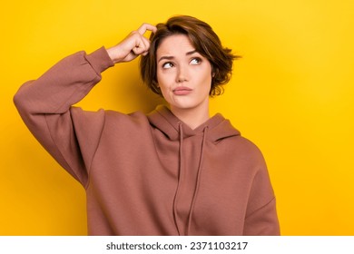 Retrato de ponder pensive girl bob cabello vestido marrón ropa deportiva arañazos su cabeza luce espacio vacío aislado en color amarillo fondo