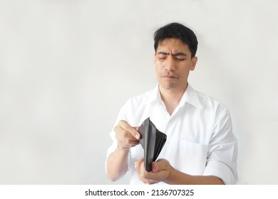 Portrait Of Poor Asian Guy Looks At His Empty Wallet, Unhappy, Worried, Lose Money, Funny Facial Expressions. Concept Of Employee, Businessman, Office Worker, Bankruptcy, And Unemployment In Crisis