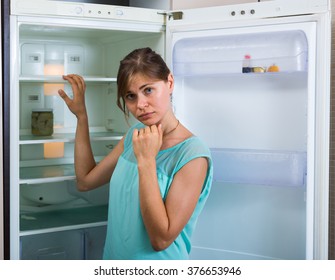 Portrait Of Poor And Upset  Girl Near Empty Fridge