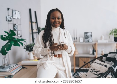 Portrait of positive African American female designer with long dreadlocks smiling and looking at camera while sitting on table at office - Powered by Shutterstock