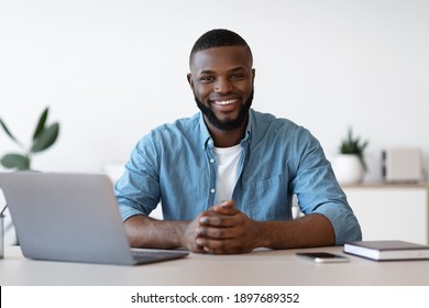 Portrait Of Positive African American Freelancer Man Sitting At Desk In Home Office. Handsome Black Guy Self-Entrepreneur Working At Table With Laptop Computer, Looking At Camera And Smiling - Shutterstock ID 1897689352