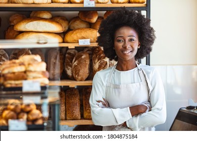 Portrait of positive African American young woman working in own Bakery shop, looking at camera with toothy smile. Pretty baker smiling at camera. Small Bakery shop owner standing in front of store - Powered by Shutterstock