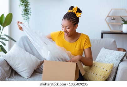 Portrait of positive african american young woman unpacking cardboard box, received delivery, moving house, sitting on the couch in living room, free space. Excited black lady unboxing carton package - Shutterstock ID 1850409235