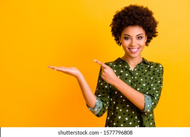 Portrait of positive afro american girl hold hand point index finger present promotion adverts recommend select choose decide advise wear stylish clothes isolated yellow color background