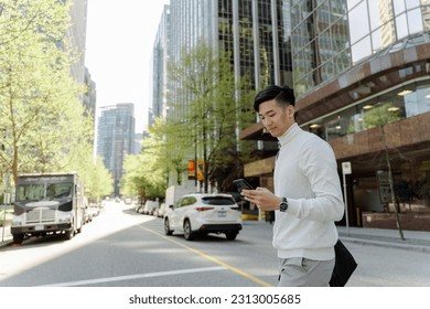 Portrait of positive asian man looking at mobile phone walking on city street. Attractive chinese student chatting, online shopping - Powered by Shutterstock