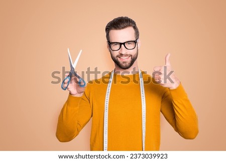 Portrait of positive cheerful dressmaker having centimeter on neck and scissors in hand showing thumb up with finger isolated on grey background. Recommend approve concept