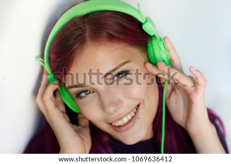 portrait of a positive and cheerful girl with purple hair looking with a smile into the camera listening to her favorite music on green headphones isolated on white background