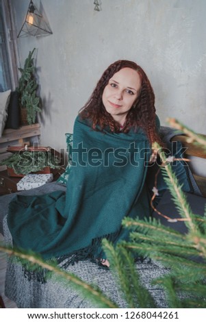 Portrait of positive cheerful girl sitting on sofa in comfortable apartment covered by plaid 
