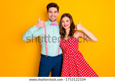 Portrait of positive cheerful spouses hug embrace show thumb up sign promote ads wear red dotted dress suspenders shirt isolated over bright shine color background