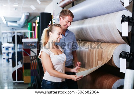 portrait of positive couple looking at linoleum flooring in interior store