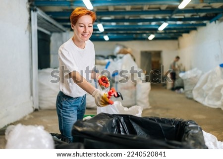 Portrait of positive female volunteer worker in latex gloves sorting diverse waste for further disposal at modern private waste recycling plant. Concept of environment protection and zero waste.
