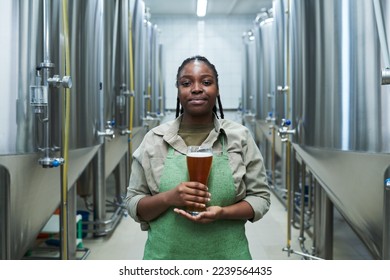 Portrait of positive female worker in uniform showing glass of beer produced in her brewery - Powered by Shutterstock