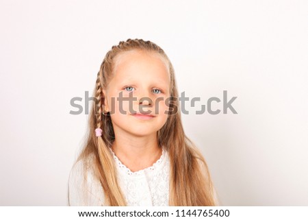 Portrait of positive and funny four year old little girl with blond hair, pigtail, dressed in white shirt smiling, satisfied facial expression. Child female, isolated background, copy space, close up.
