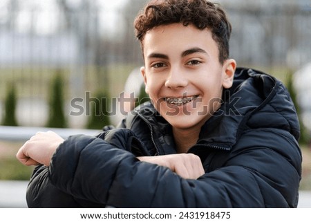 Portrait of positive happy boy, handsome teenager with braces looking at camera, wearing casual outfit standing on urban street. Advertisement concept, dental care 