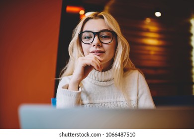 Portrait of positive hipster girl in eyeglasses for vision correction working on freelance using laptop computer, female student satisfied with e learning course getting knowledge online on netbook