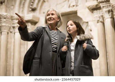 Portrait of positive intelligent senior woman and cute interested preteen girl viewing ancient sculptures in museum
