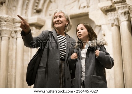 Portrait of positive intelligent senior woman and cute interested preteen girl viewing ancient sculptures in museum