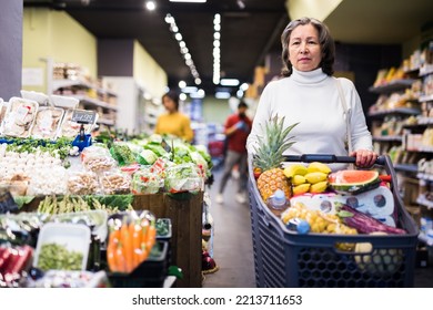 Portrait of positive interested elderly woman visiting supermarket food department for shopping