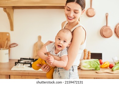 Portrait, Positive Loving Caucasian Woman, Mother Playing With Baby At Home On Weekends, Mom Holding Son In Her Arms, Playing Together And Having Fun, Standing In Modern Kitchen.