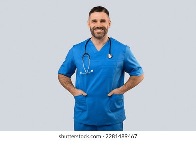 Portrait of positive male doctor or nurse posing with hands in pockets and smiling at camera isolated over grey studio background, male wearing blue coat and stethoscope - Powered by Shutterstock