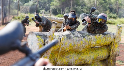 Portrait of positive male and female paintball players in full gear playing outdoors. Focus on man