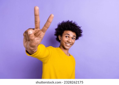Portrait of positive nice man beaming smile good mood arm fingers demonstrate v-sign isolated on purple color background