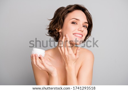 Portrait of positive pretty girl prepare dating look in mirror apply new skin care cream on her face to make face soft fresh nature isolated over grey color background