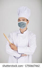 Portrait Of Positive Restaurant Chef In Medical Mask Holding Wooden Spoon