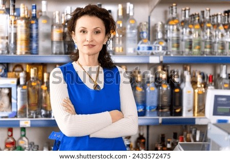 Portrait of positive saleswoman at cash register of a liquor store