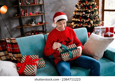 Portrait of positive satisfied young man sitting comfort sofa hold festive giftbox open ribbon bow fairy spirit apartment inside - Powered by Shutterstock