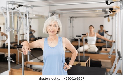 Portrait of positive smiling elderly woman standing leaning on wunda chair in pilates studio ready for training. Healthy and active lifestyle of seniors concept - Powered by Shutterstock