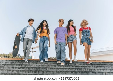 Portrait of positive smiling multiracial teenagers wearing stylish casual colorful t shirts, holding skateboard, walking down stairs on street. Happy young hipsters meeting together - Powered by Shutterstock