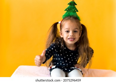 Portrait of positive smiling surprised happy little schoolgirl girl Christmas tree decoration on head polka dot dress show thumbs up orange background. New year, holiday, celebration, winter concept - Powered by Shutterstock