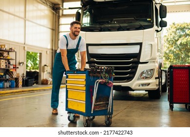 Portrait of positive smiling truck serviceman with tools standing by truck vehicle in workshop. Truck vehicle maintenance and servicing. - Powered by Shutterstock